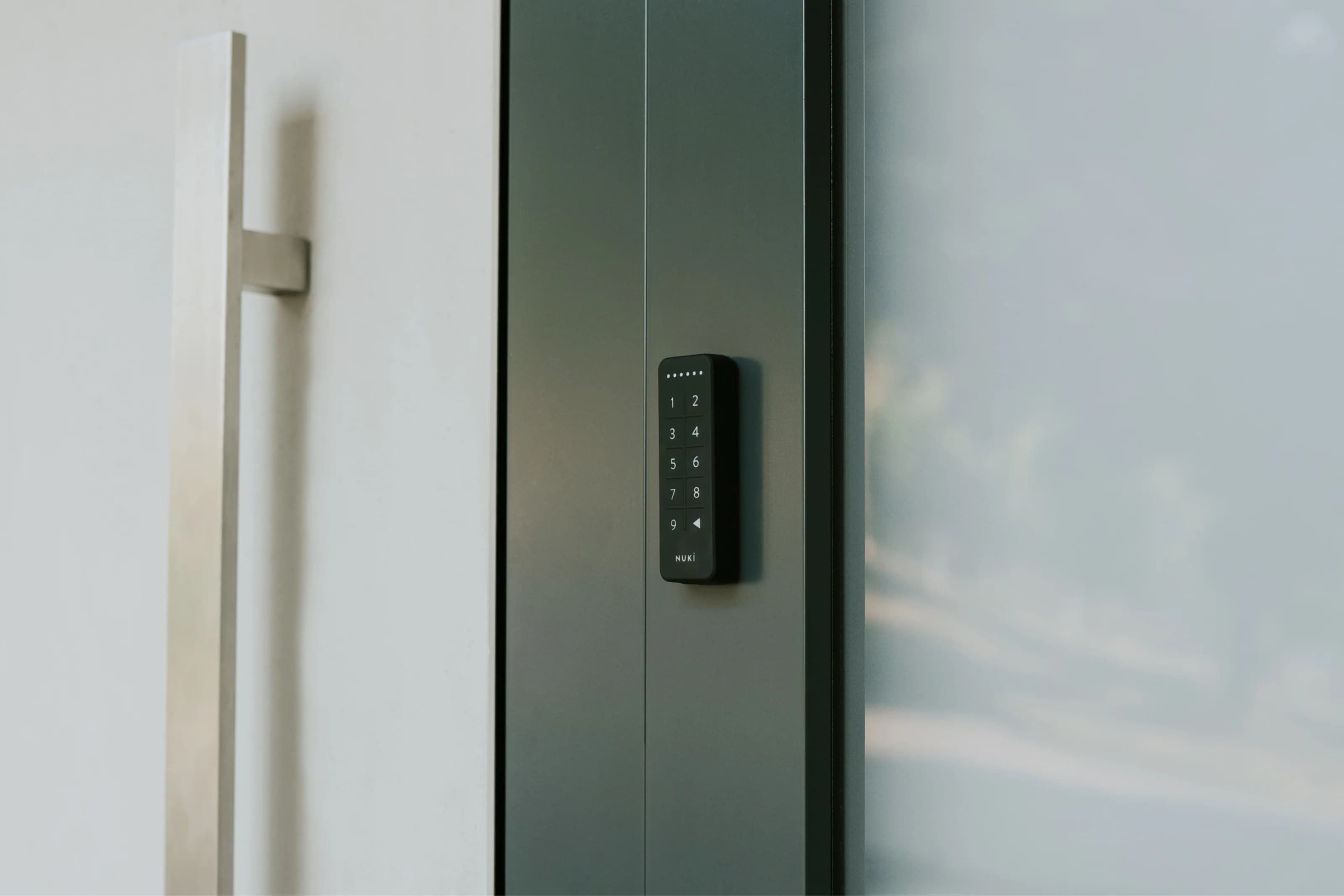 Modern bir ev kapısının yanına monte edilmiş Nuki Keypad ile anahtarsız giriş