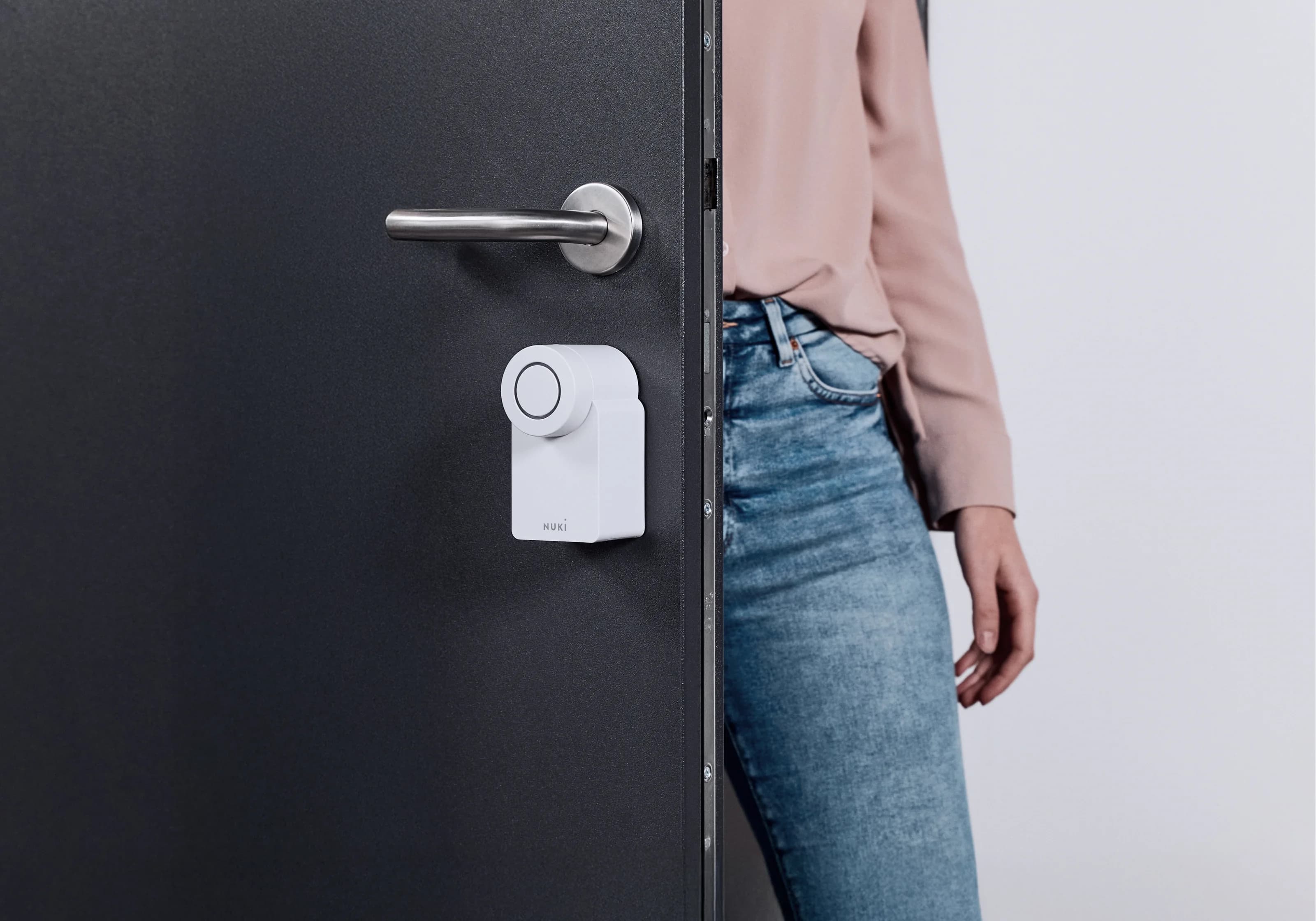 Nuki Smart Lock Go takılı bir kapının yanında duran kadın: sade tasarımlı akıllı erişim